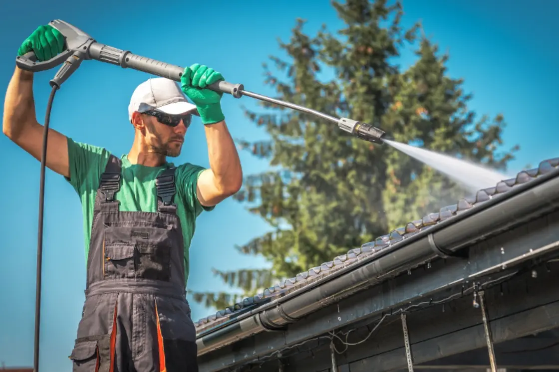 Person using a pressure washer to clean gutters