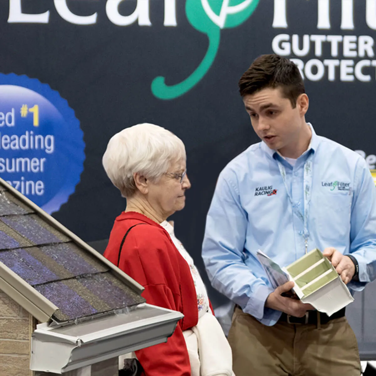 A LeafFilter representative holds and explains a LeafFilter-protected gutter to an attendee at a home show