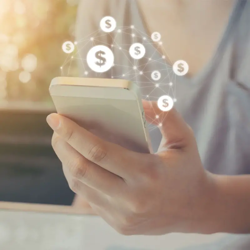 A woman in a gray shirt holds a smart phone with an animated icon of webbed dollar signs protruding from its screen