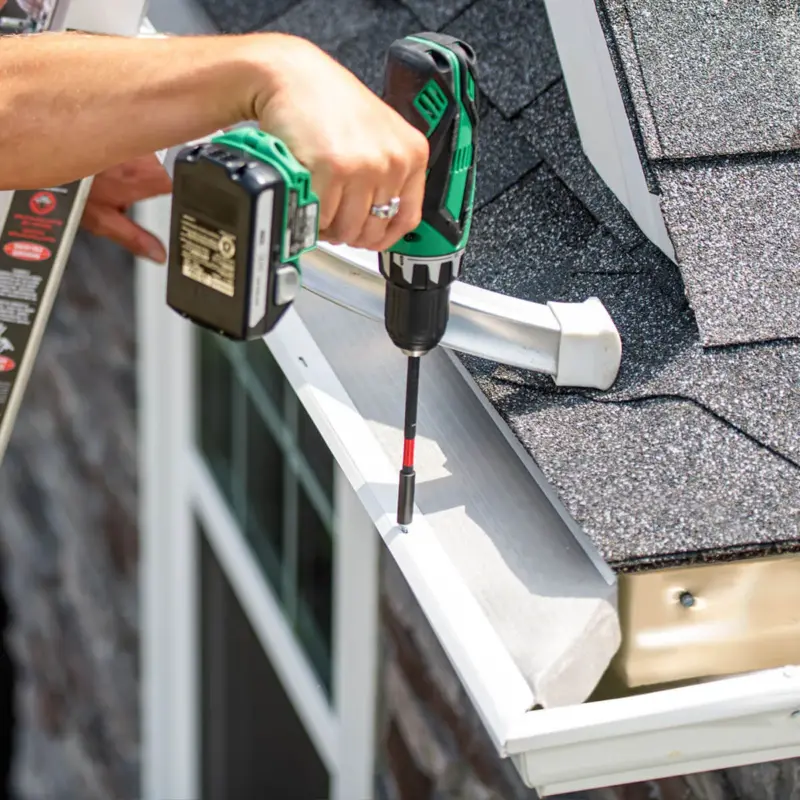 A LeafFilter installer situates gutter protection on clean, white gutters and secures it with a cordless power screwdriver.