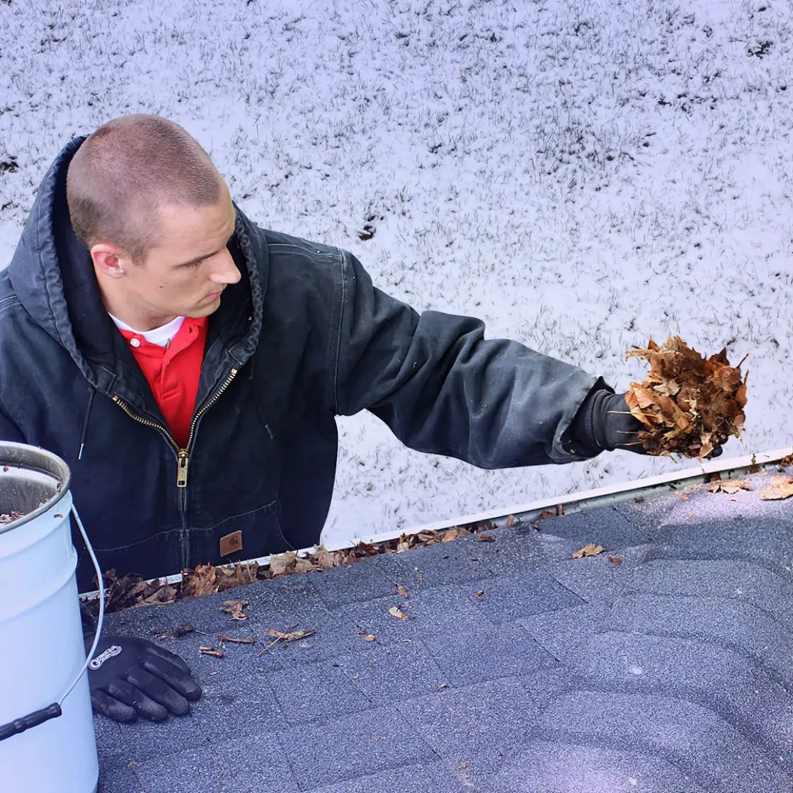 A gutter cleaner perches alongside a roof to clean gutters. Snow covers the grass in the background.