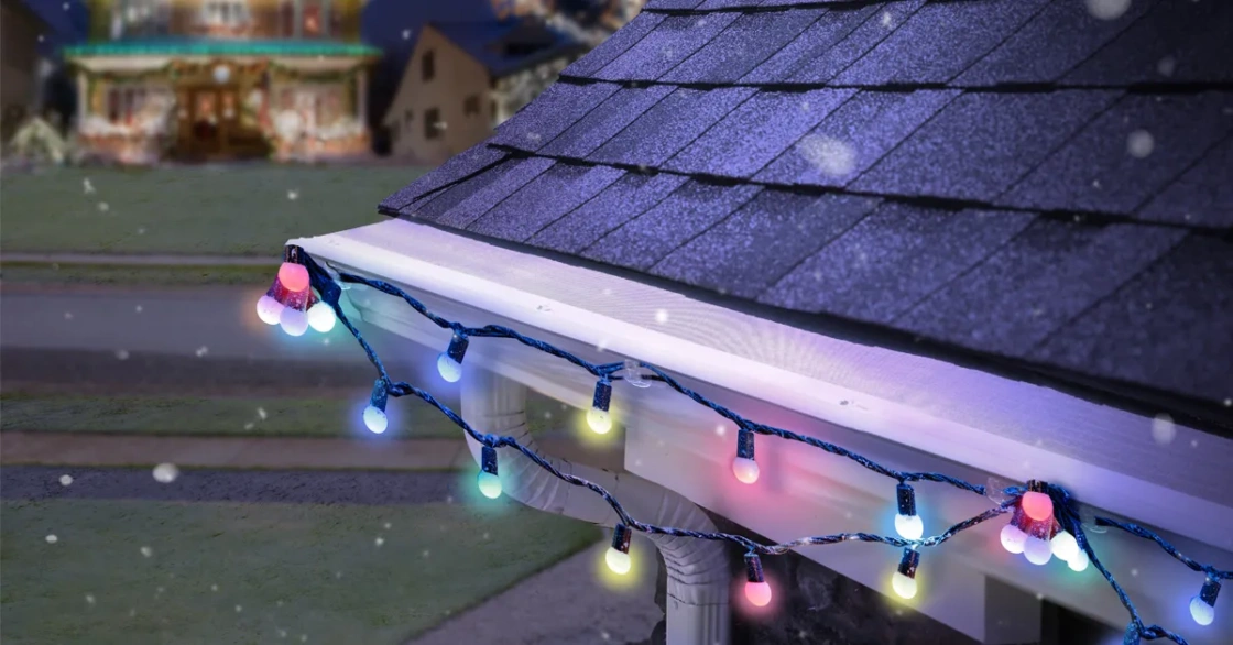 LeafFilter is installed on white gutters with a festive light strand hung on it. Snowflakes fall in the foreground.