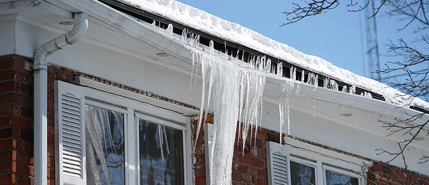 An icicle overflows past clogged gutters, causing them to sag