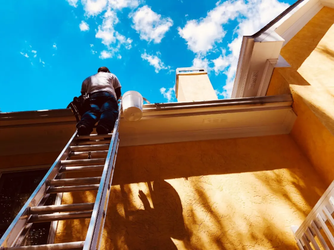 Person standing on a ladder to reach a home's second story gutters