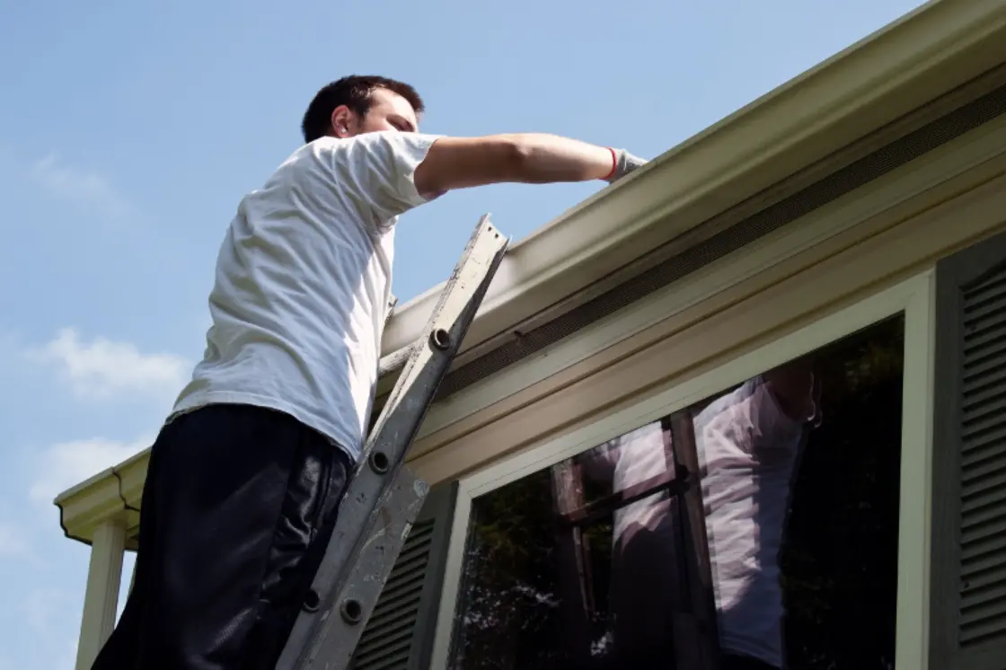 Person on a ladder cleaning a home's gutters