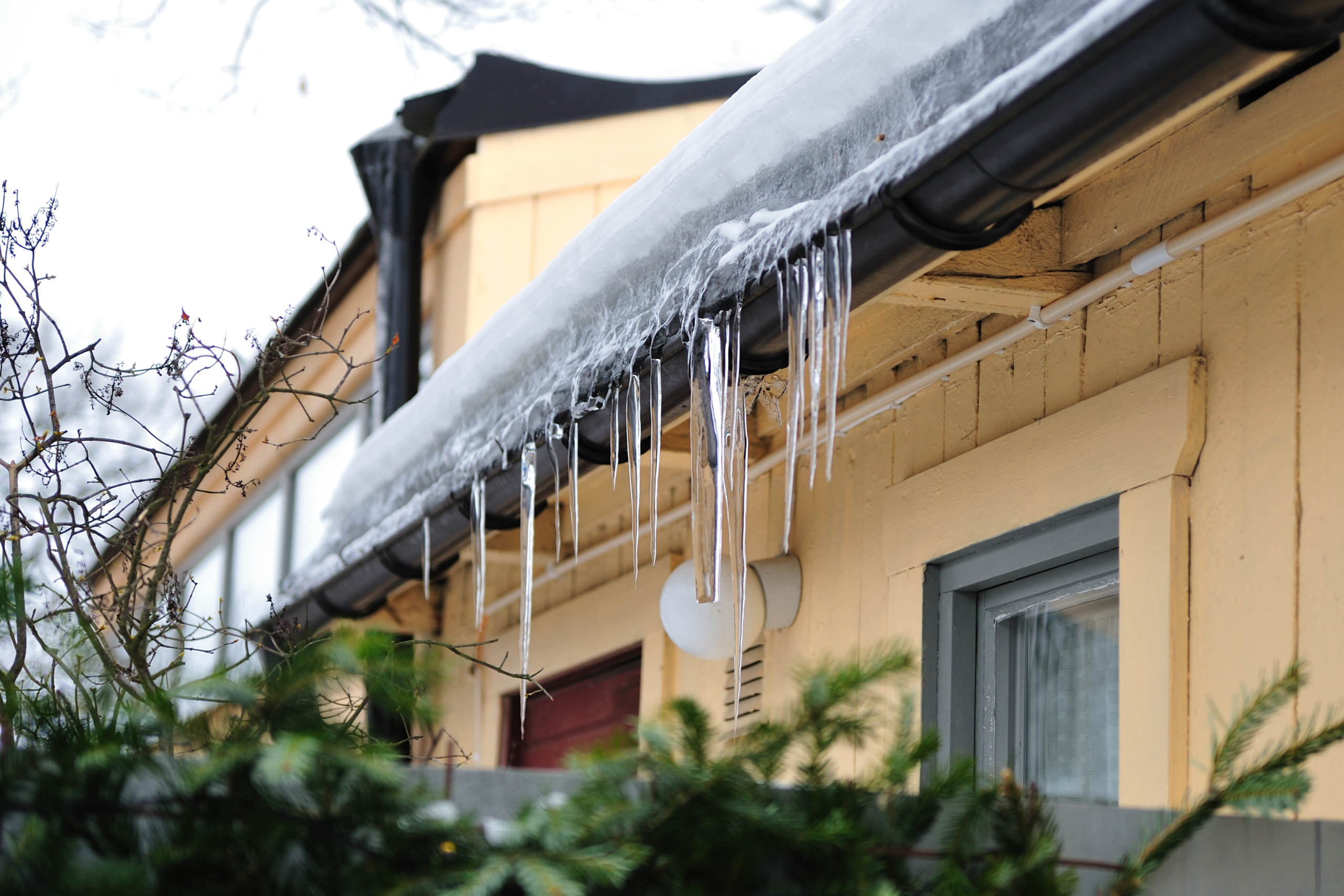 Side of a home with snow and ice dams on the roof and in gutters. 