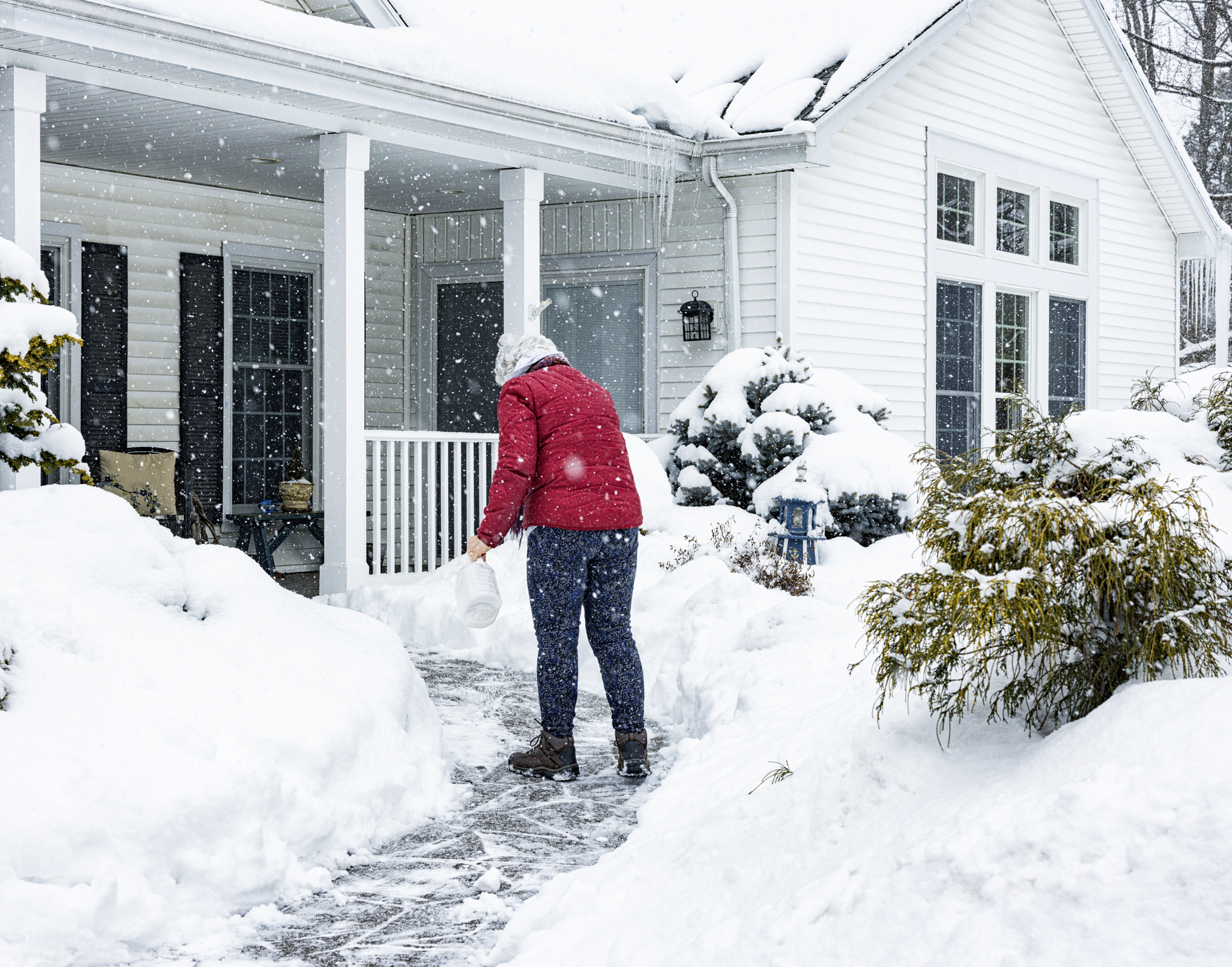 Woman sprinkling de-icing salt on home's front walkway to winterize your home.