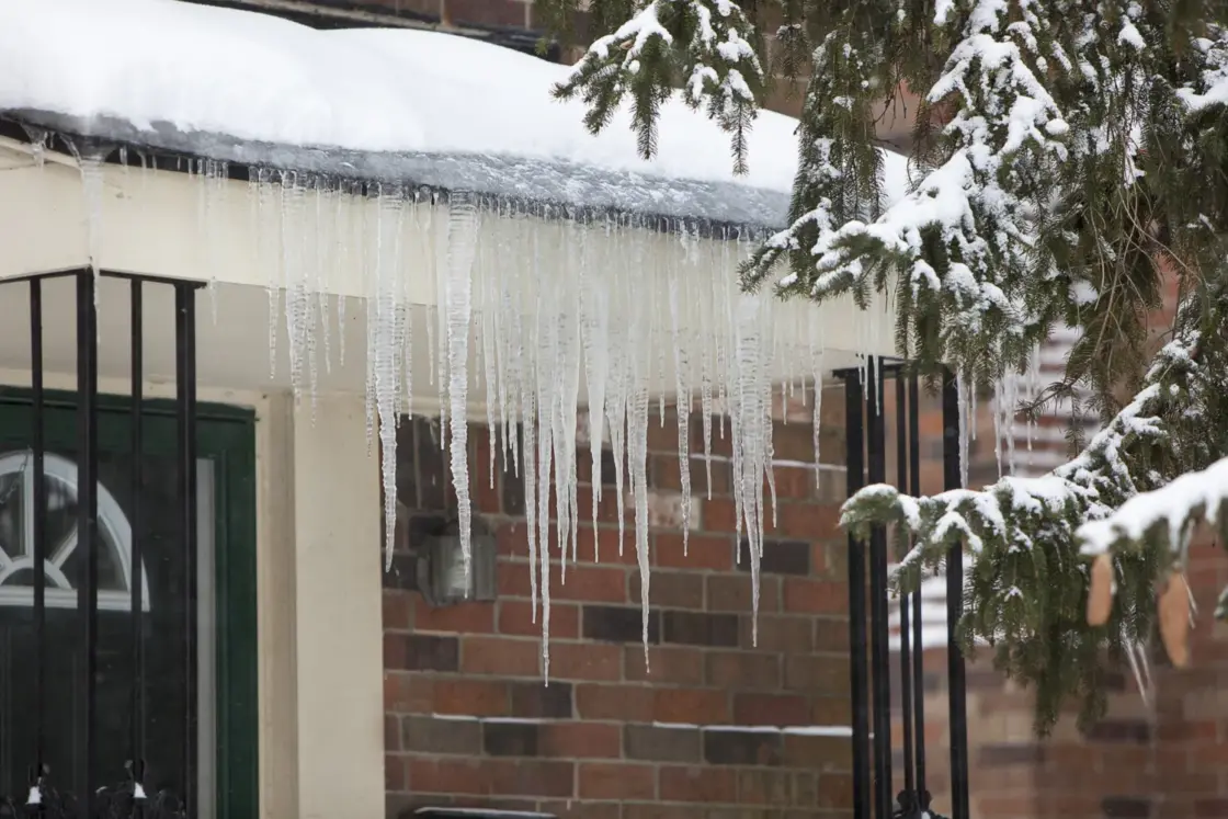 Home roof winter gutter guards with snow and icicles hanging