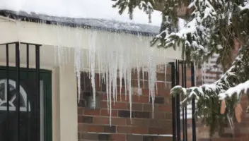 Home roof winter gutter guards with snow and icicles hanging