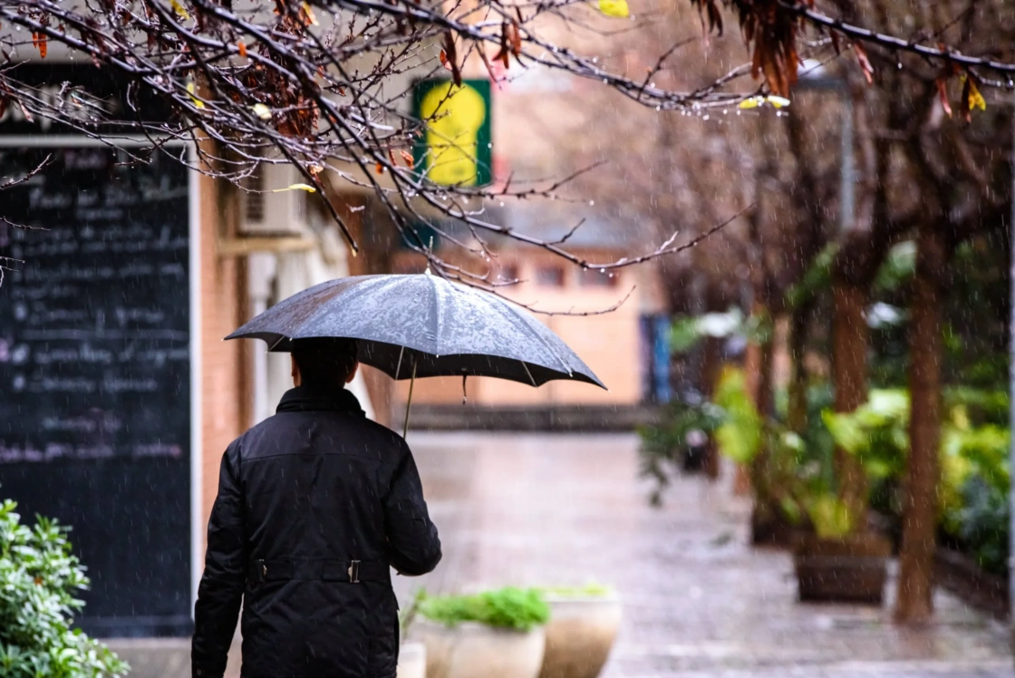 An adult man walked down the street of a city with a black umbrella on a rainy day.