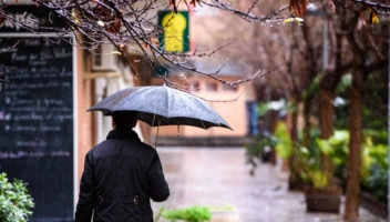 An adult man walked down the street of a city with a black umbrella on a rainy day.