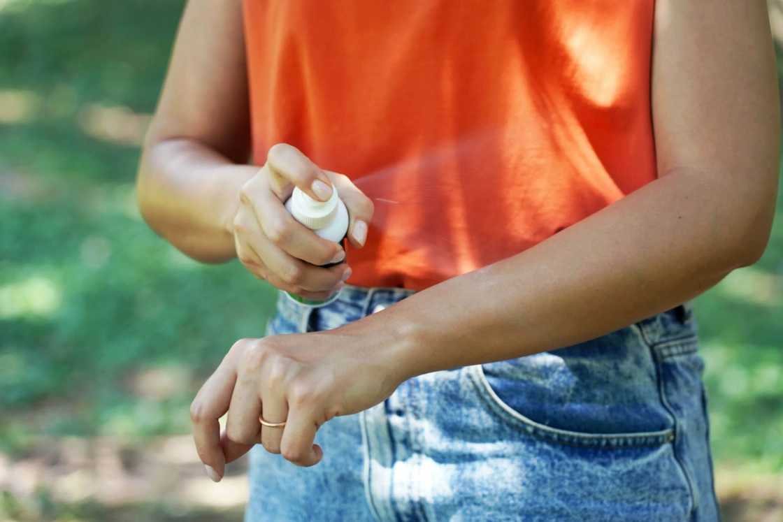 Girl spraying insect repellent on her arm outdoor in nature using spray bottle.