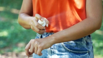 Girl spraying insect repellent on her arm outdoor in nature using spray bottle.