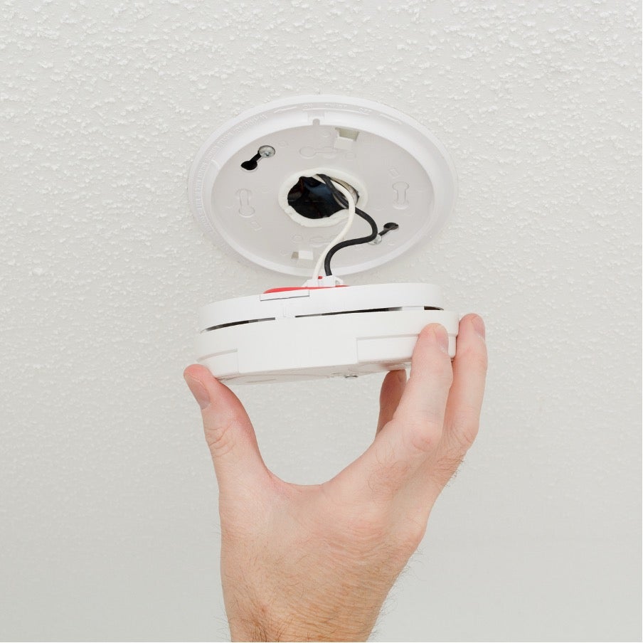 Closeup man's hand unscrewing ceiling smoke detector checking off item on home maintenance checklist
