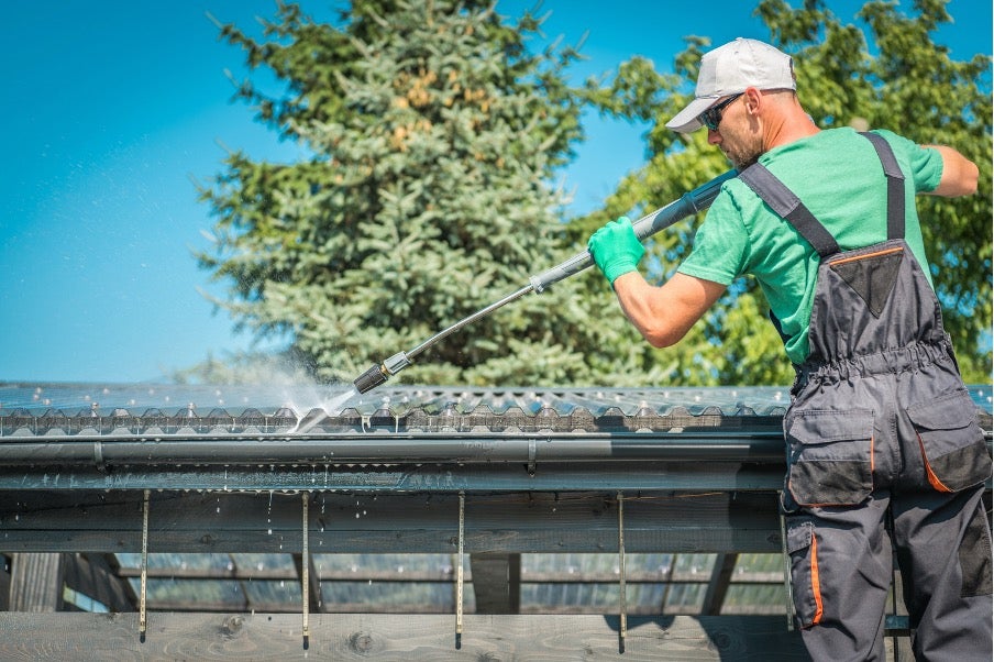 man on ladder power washing spring gutters.