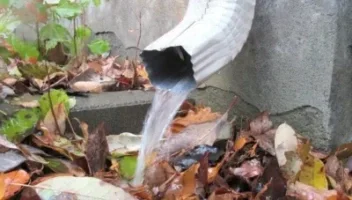 close up white downspout with water coming out next to home foundation. downspout sizes and materials