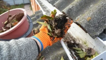 close hand with orange glove cleaning out dirty gutter why gutters are important in the southeast