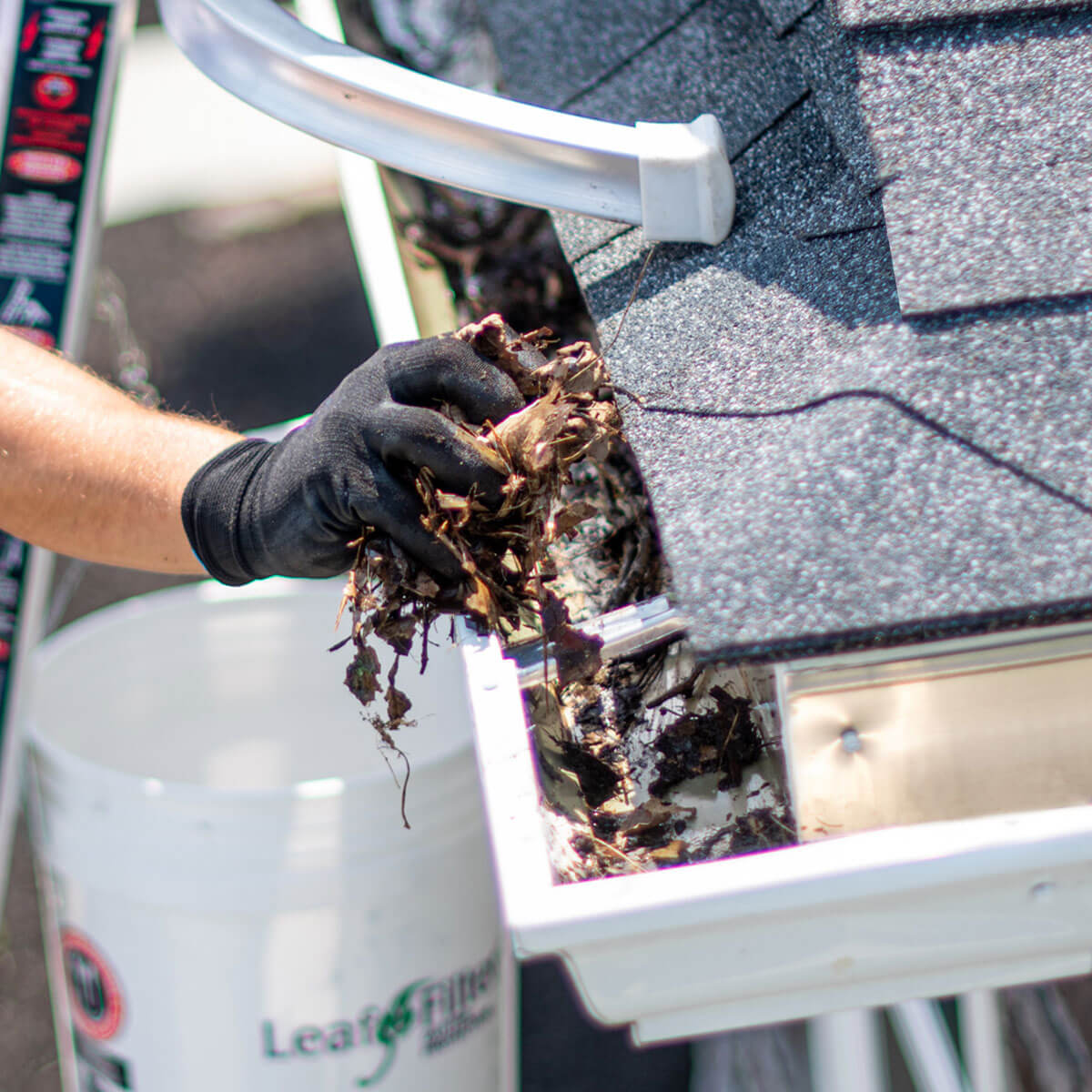 A LeafFilter installer cleans debris from clean, white gutters and places it in a white branded buckets.