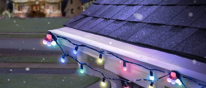LeafFilter is installed on white gutters with a festive light strand hung on it. Snowflakes fall in the foreground.
