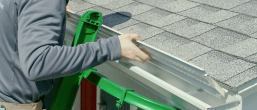 A worker in a gray hoodie and khakis installs LeafFilter on white k-style gutters