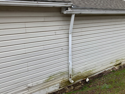 A side of a house showing broken gutters, broken downspout and mold damage